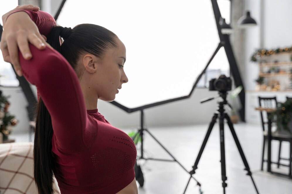 A female fitness model taking part in a session, with a camera and photographic equipment in the background.
Source: Freepik