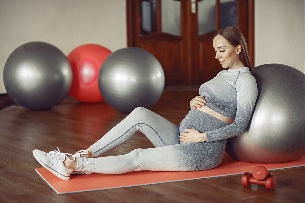 A pregnant woman sitting on a fitness mat with one big fitness ball and some more in the background. 
Source: Freepik