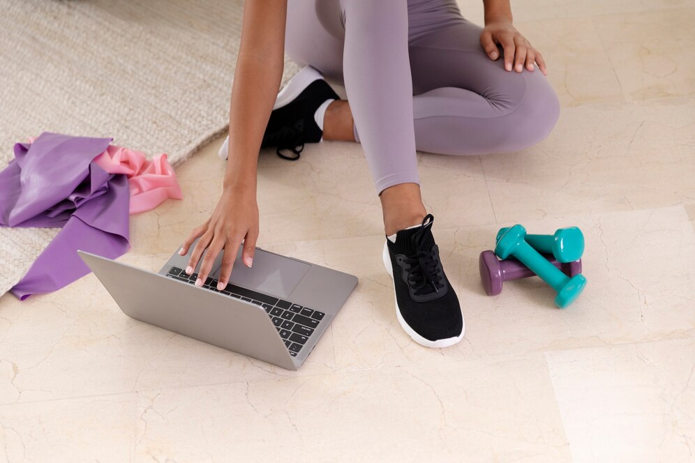 A female personal trainer working with her computer, having fitness equipment around - carpet, gums and dumbbells.
Source: Freepik