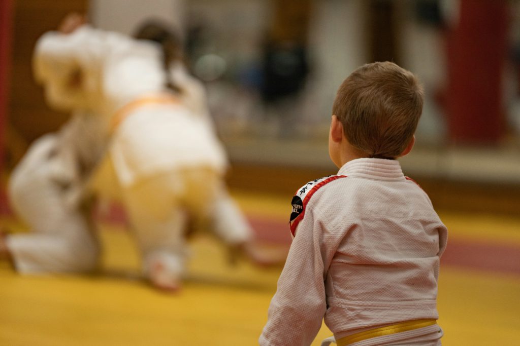 A young boy wearing martial arts clothes, watching older competitors and feeling this is his life goal.