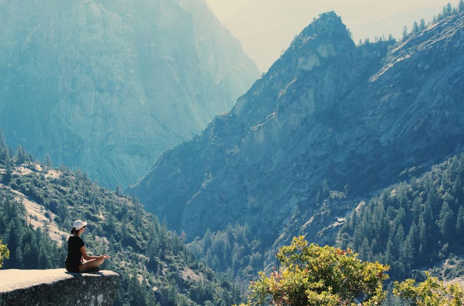 A beautiful mountain view and a girl meditating on a rock as a symbol of the location of a yoga studio.