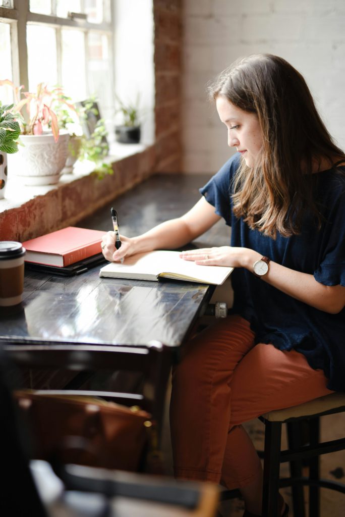 A woman writing notes connected with her plan for a yoga business, in a good-vibe surrounding.