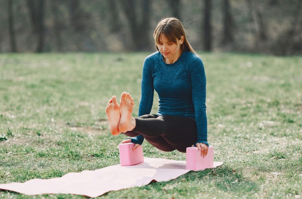 A young lady practicing on a meadow on a yoga mat and with yoga blocks, one of the stretching yoga equipment.