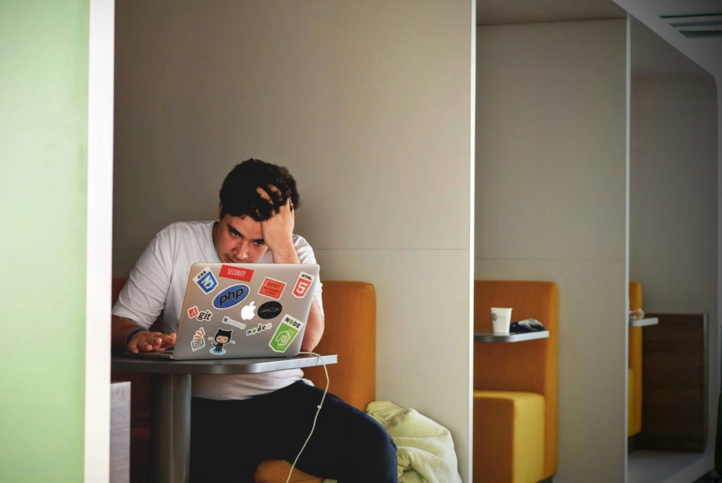 A frustrated man sitting in front of his laptop, to illustrate dependence and lack of creativity when having a franchise gym.