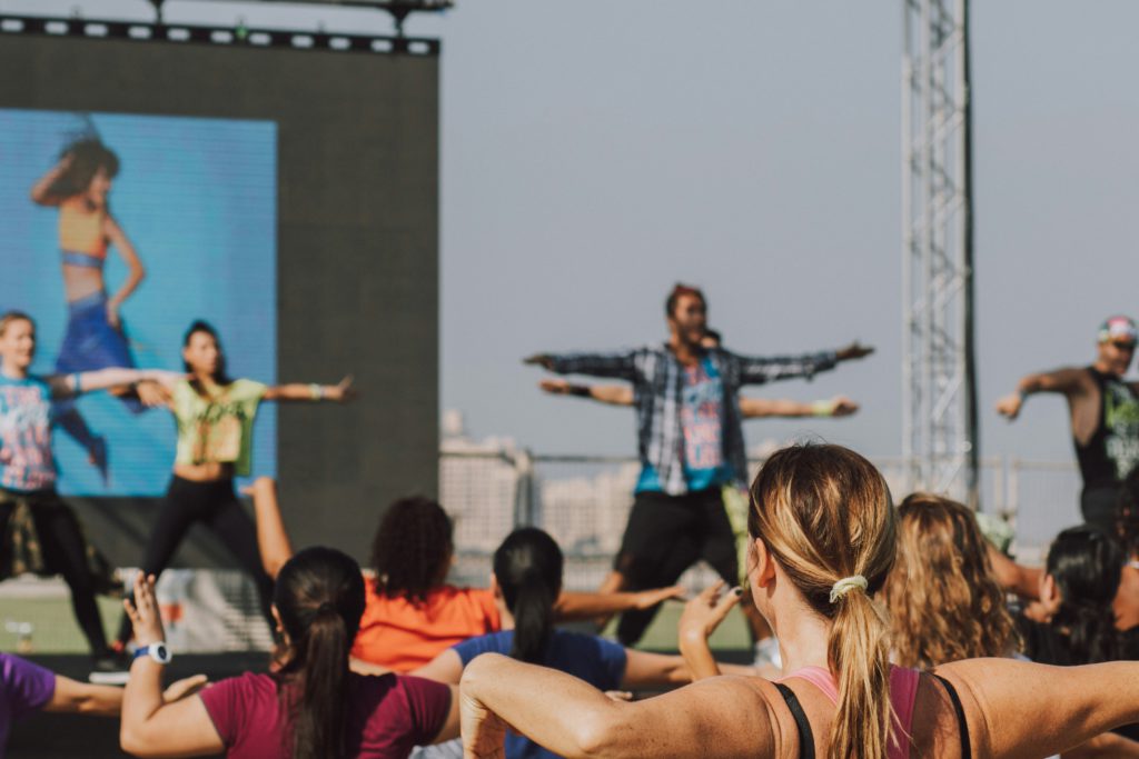 Sample fitness classes for a crowd standing in front of a high stage.