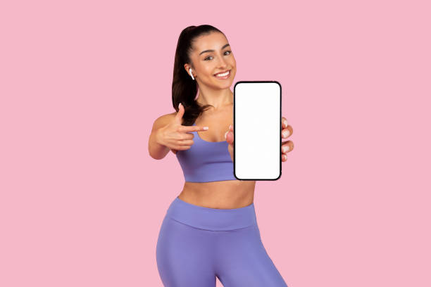 A smiling woman, dressed in fitness clothes, showing her phone where she displays social media posts from her gym.