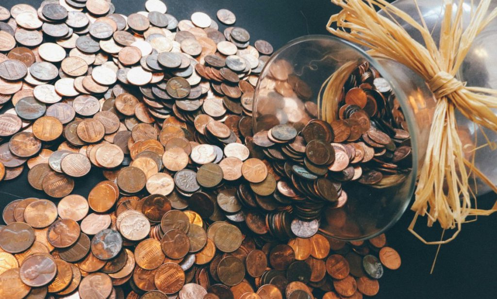 Multitude of coins falling out from a glass vase, as a symbol of yoga studio marketing costs.