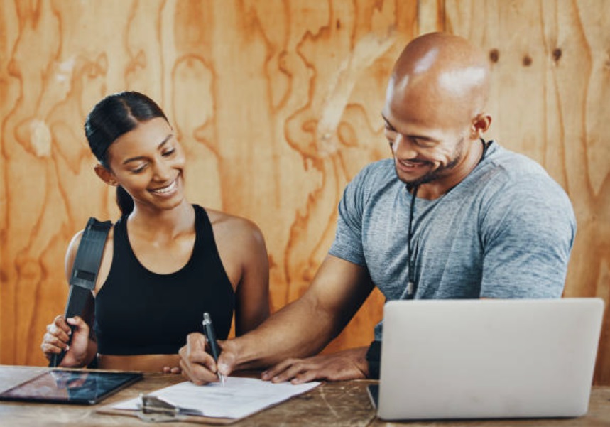 A newly hired personal trainer is signing his contract with the gym owner.