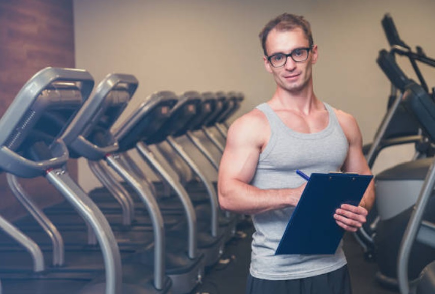 A candidate holding his gym manager resume in a personal training room.