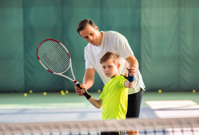 A coaching session for kids: a tennis coach working patiently with a boy.